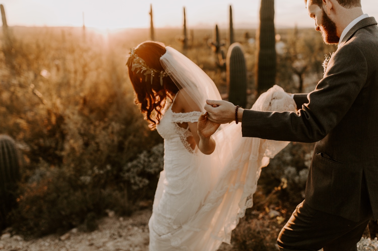 The groom helping his bride walk into the desert sunset.