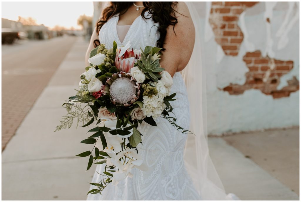 Bride holding her boho desert inspired bridal bouquet with pink protea, cactus, succulents, and flowing greenery 