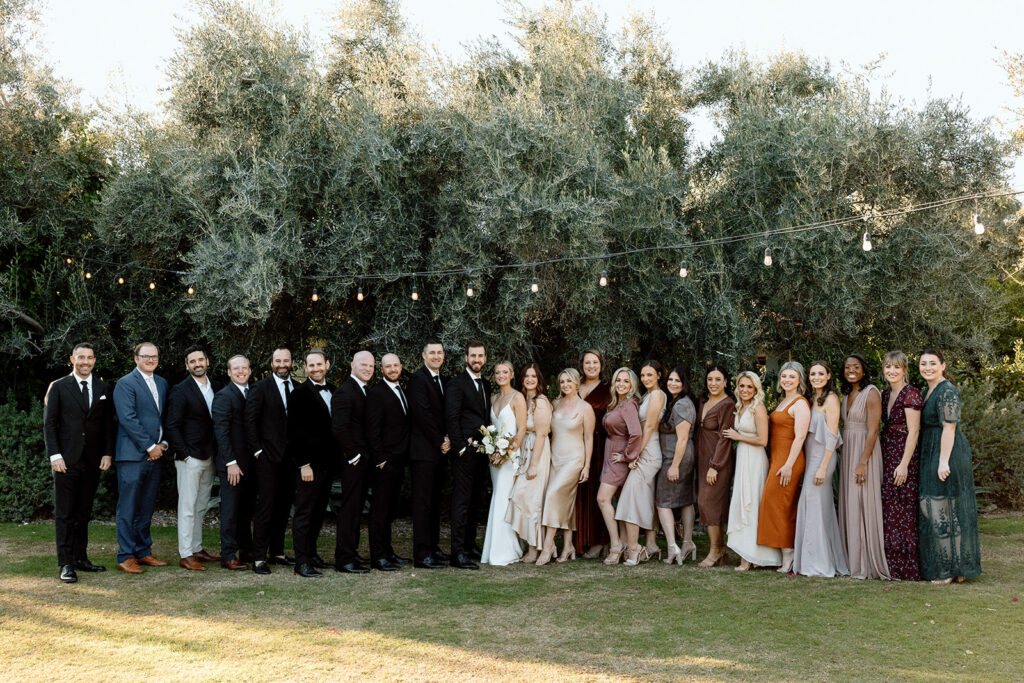 The bride and groom stand with their respective parties in a large green space to celebrate their wedding in Arizona