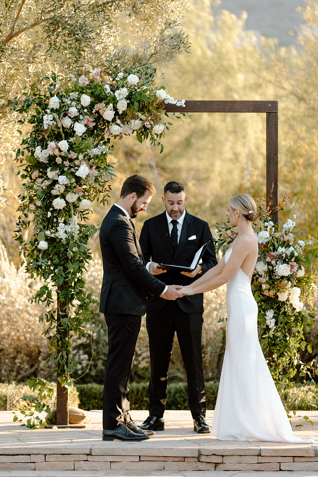 Bride and groom join hands at their beautiful floral altar at wedding venue El Chorro