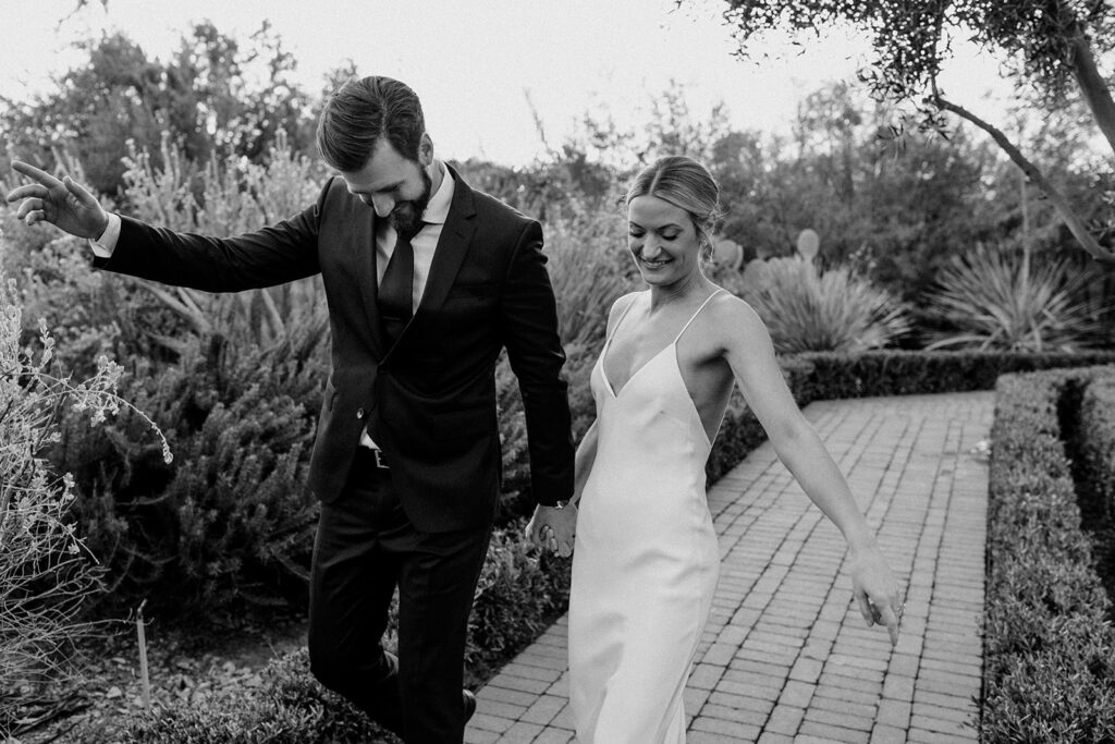 Black and white photo of a couple strolling down a brick pathway with joy on their wedding day